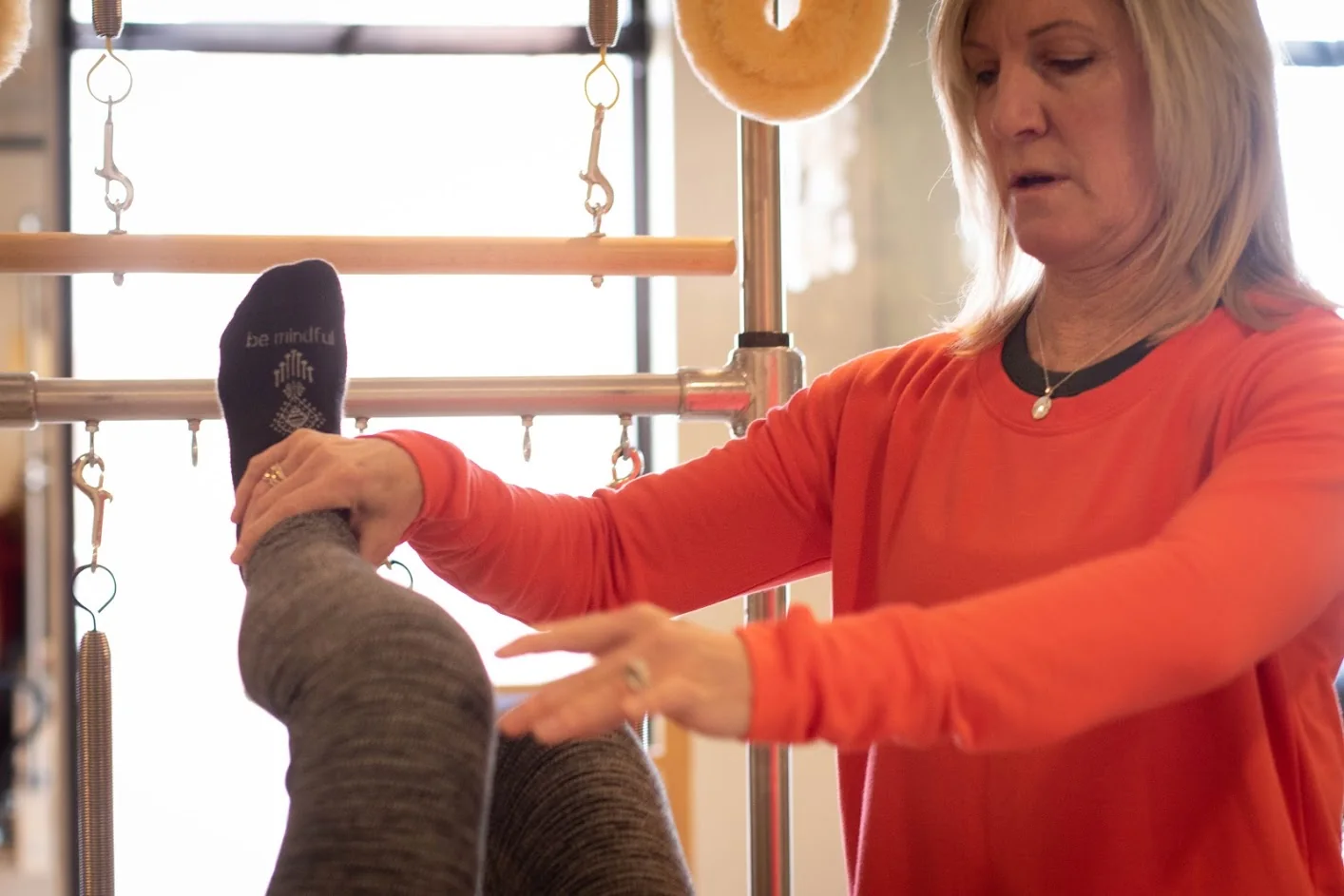 An instructor offers hands-on guidance during a seated Pilates exercise
